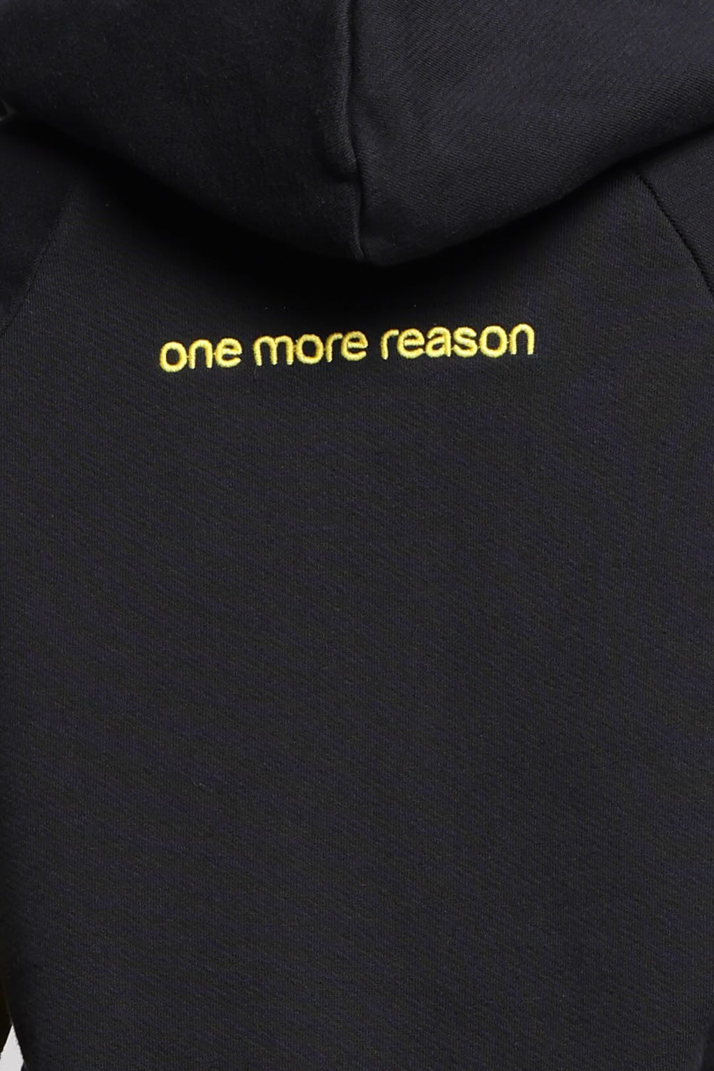 Close-up of a black hoodie with the logo 'one more reason' printed in yellow lowercase letters, from One More Reason, the European Premium Sportswear Brand.