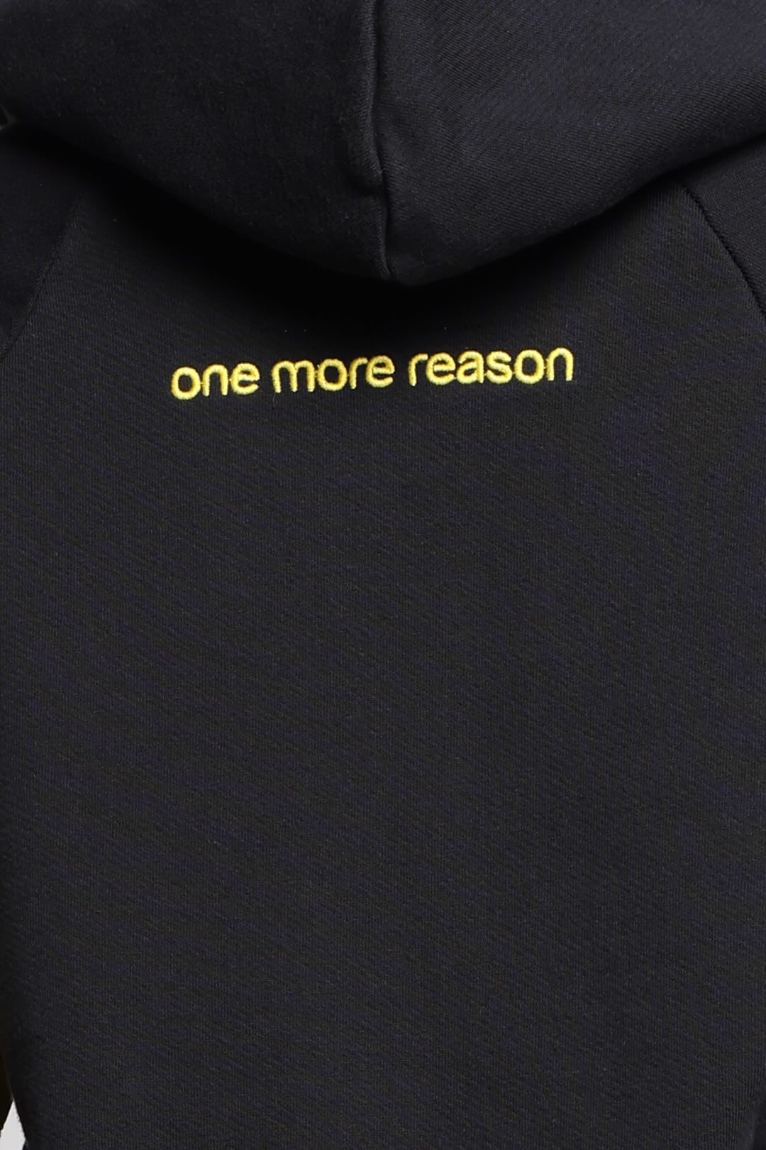 Close-up of a black hoodie with the logo 'one more reason' printed in yellow lowercase letters, from One More Reason, the European Premium Sportswear Brand.