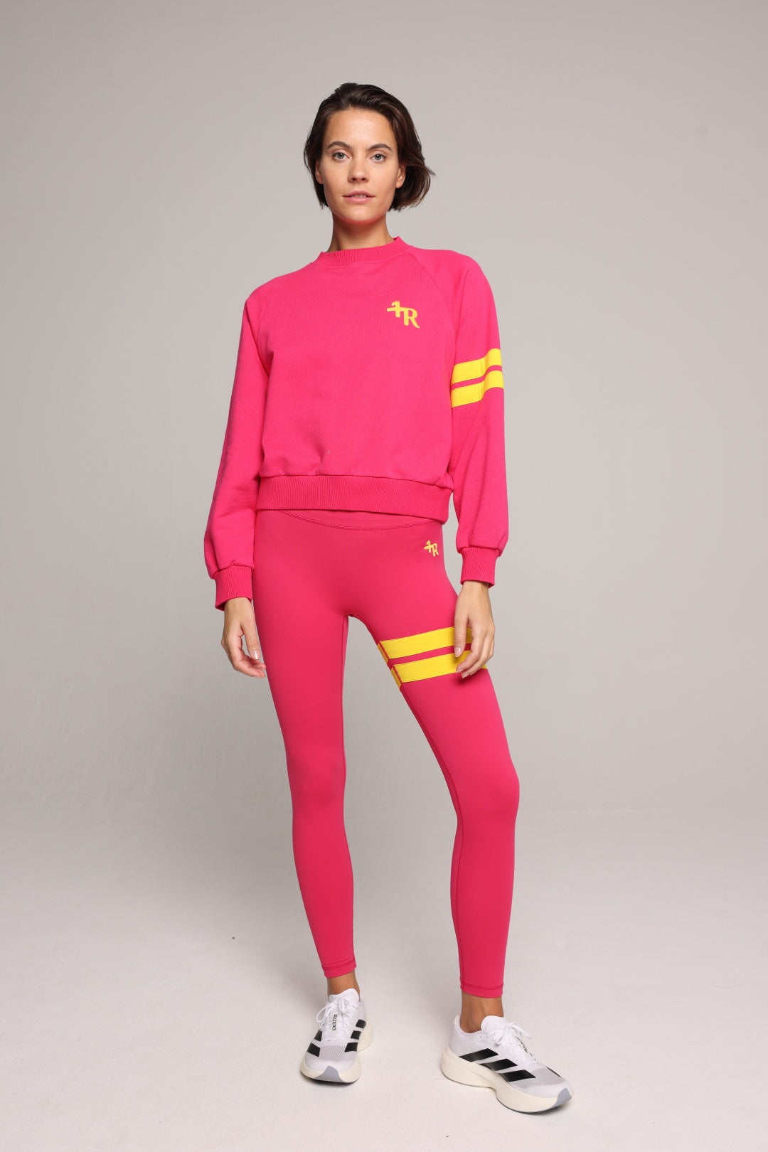 A woman wearing a bright pink sweater and leggings with yellow stripes by One More Reason, the premium sportswear brand made in Europe in a studio setting 