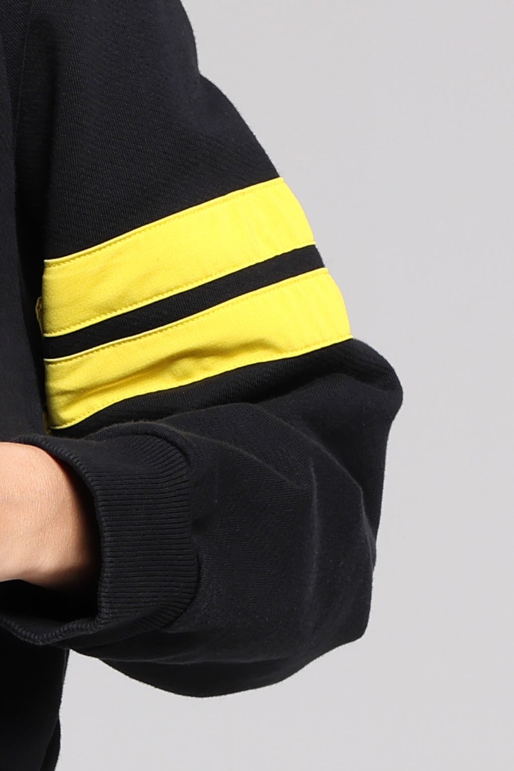 Close-up of a black sweatshirt sleeve featuring two yellow stripe on the upper arm from One More Reason, the European Premium Sportswear Brand.