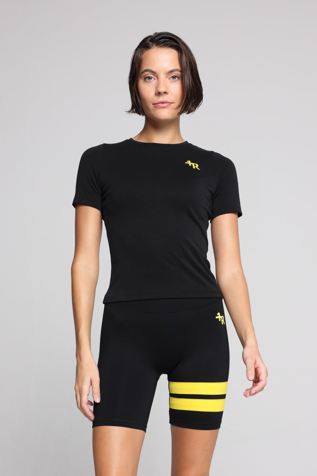 Woman wearing a black t-shirt and black shorts with yellow stripes by one more reason studio set 