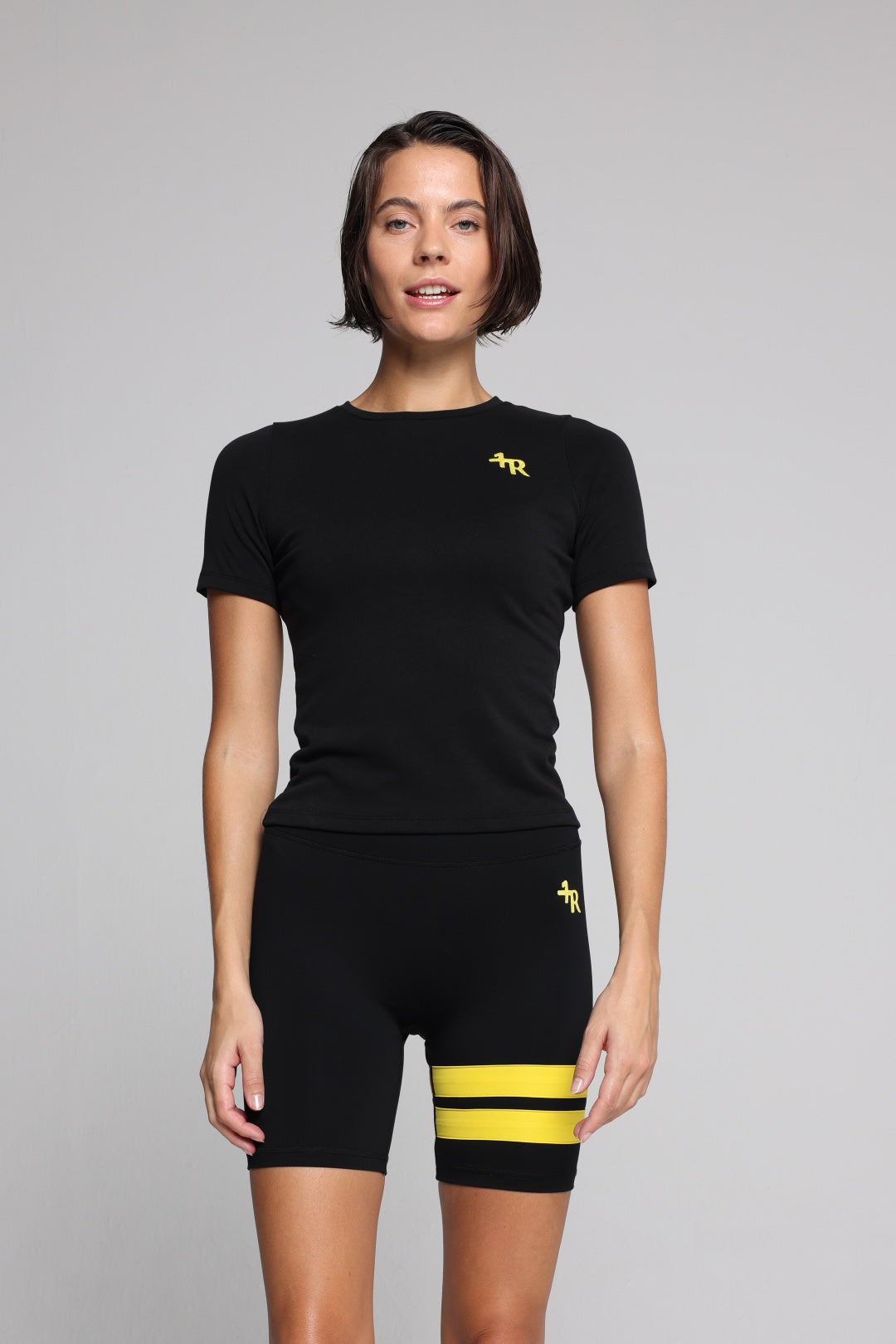 Woman wearing a black t-shirt and black shorts with yellow stripes by one more reason studio set 
