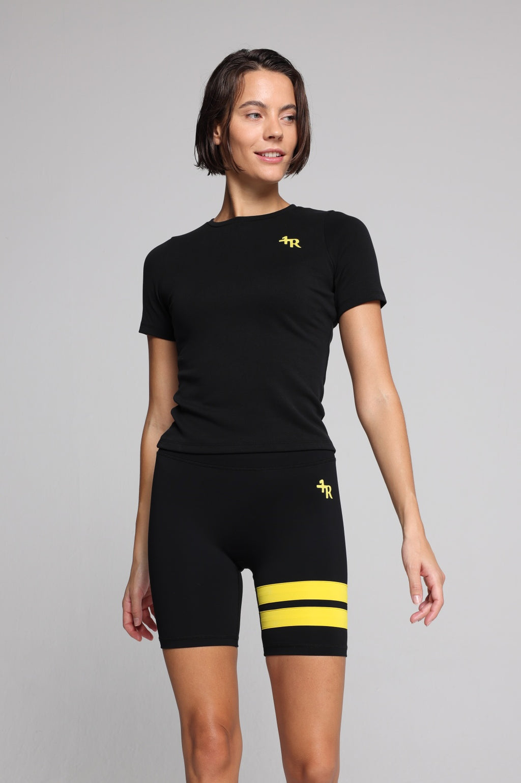 Woman wearing a black t-shirt and black shorts with yellow stripes by one more reason studio set 