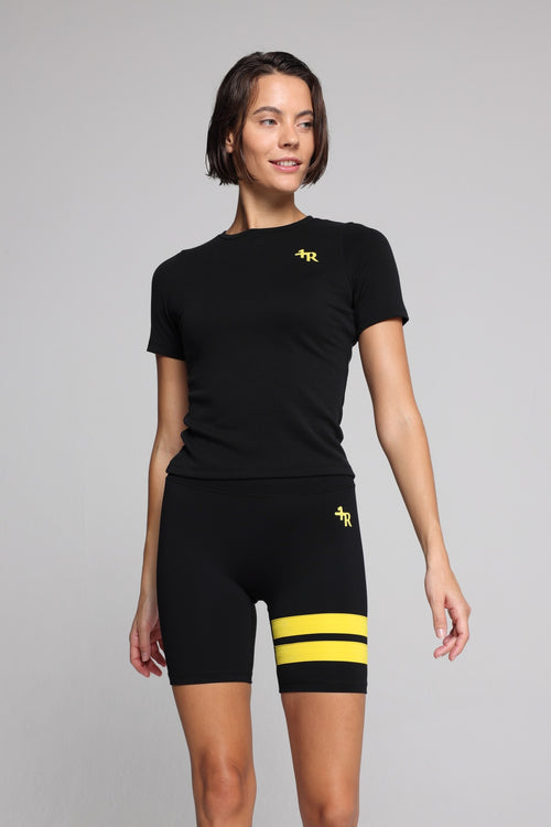 Woman wearing a black t-shirt and black shorts with yellow stripes by one more reason studio set 