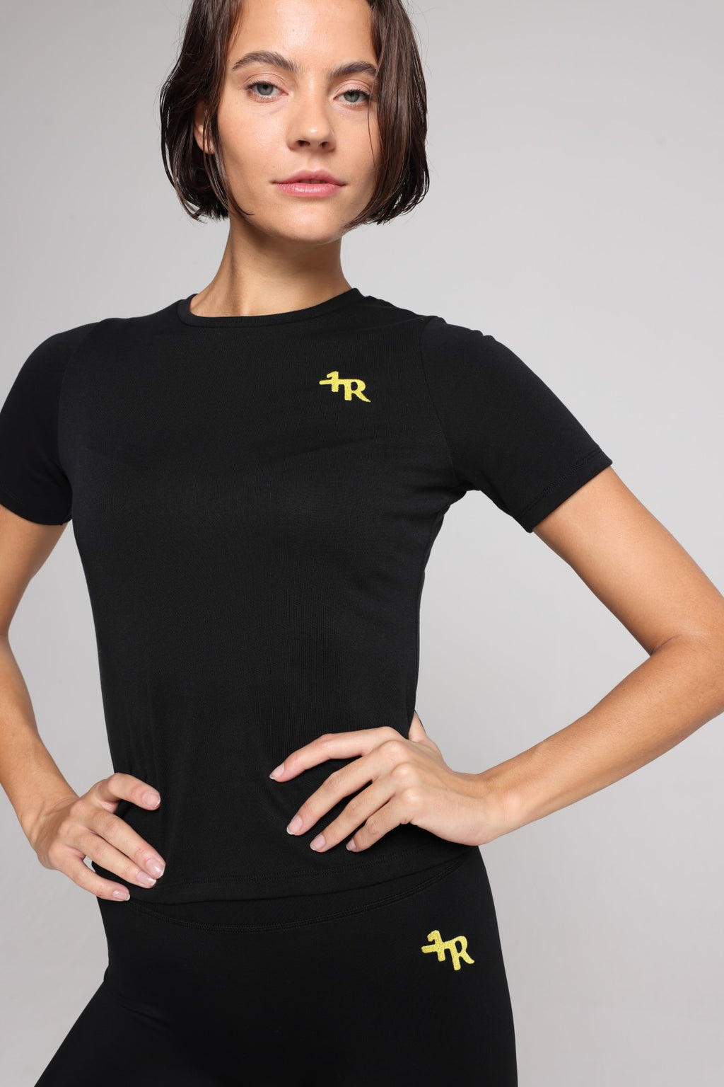 Woman wearing a black t-shirt and black shorts with yellow stripes by one more reason studio set 
