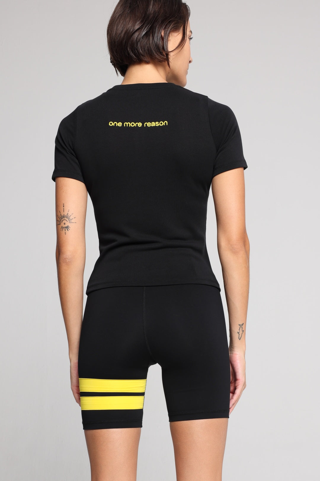 Woman wearing a black t-shirt and black shorts with yellow stripes by one more reason studio set back view