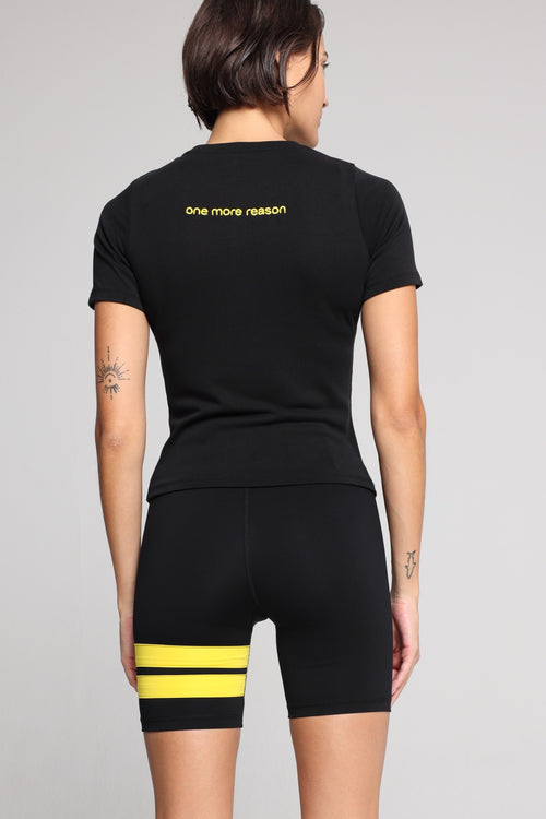 Woman shown from the back wearing a black t-shirt and black shorts with yellow stripes by One More Reason, the European premium sportswear  brand.