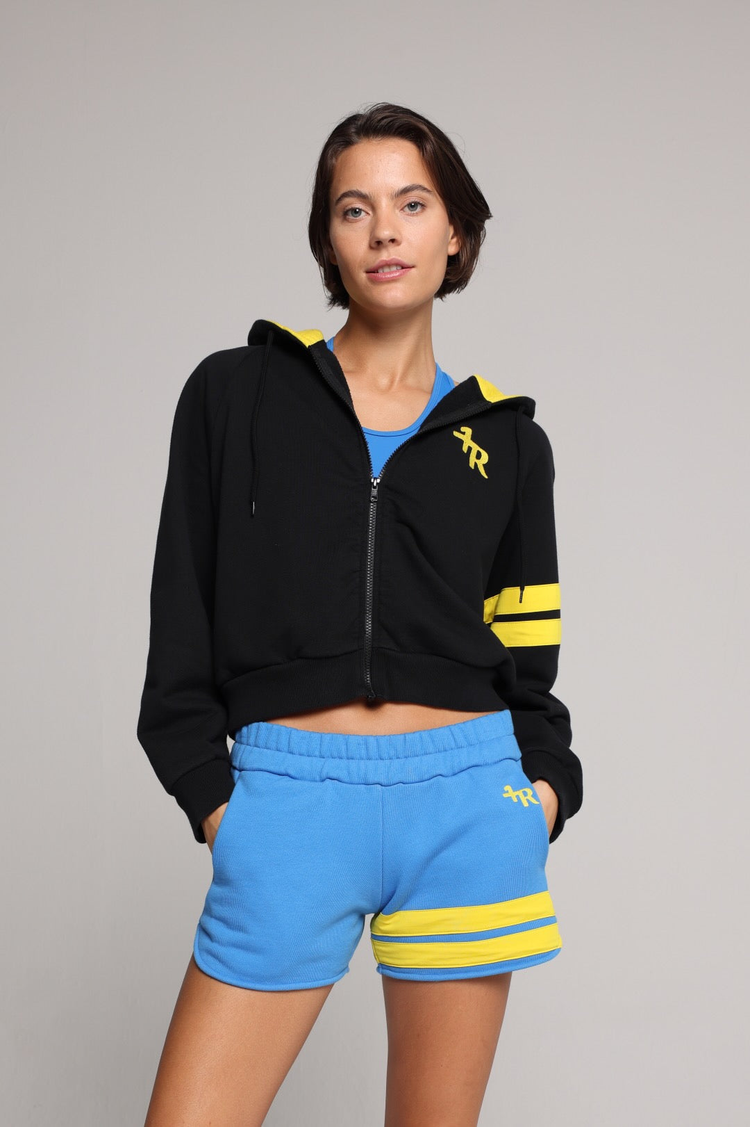 Woman wearing a black hoodie with yellow stripes and blue shorts by one more reason studio set