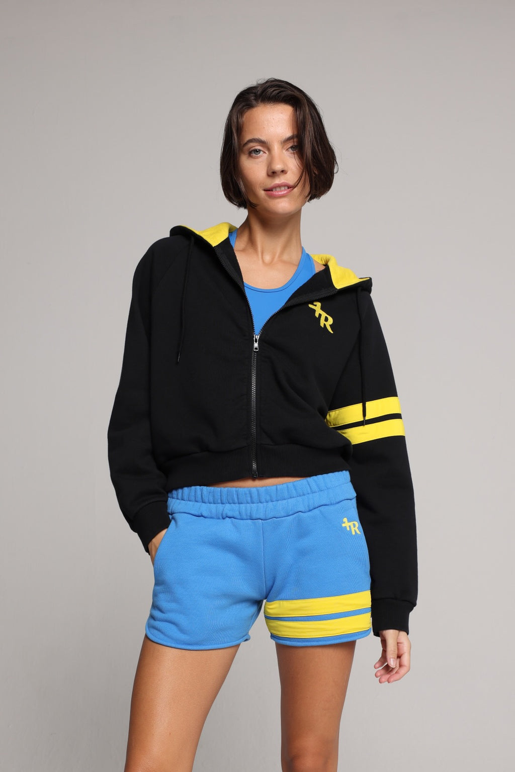 Woman wearing a black hoodie with yellow stripes and blue shorts by one more reason studio set