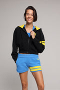 Woman wearing a black hoodie with yellow stripes and blue shorts. All from One More Reason, the European Premium Sportswear Brand.