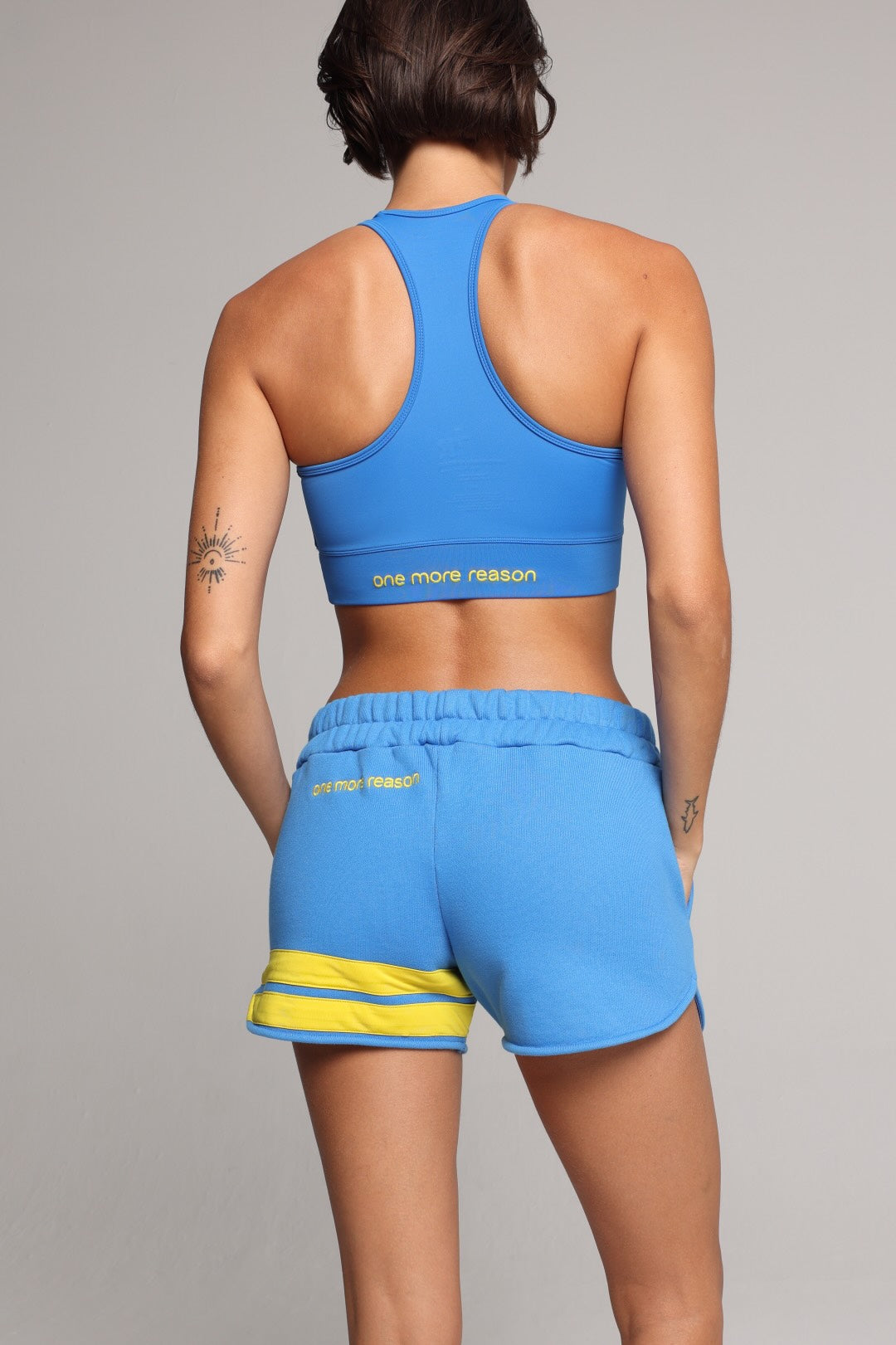 woman wearing blue cotton shorts with yellow stripes and blue tank top by one more reason premium sportswear studio set back view