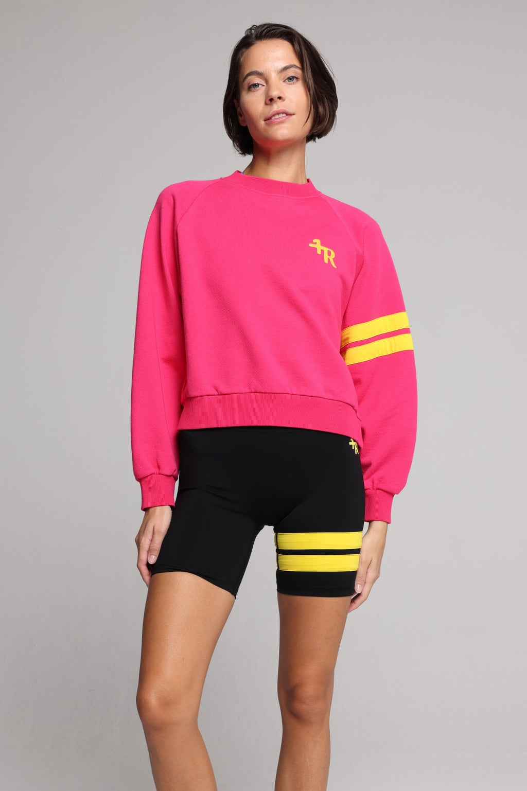 woman wearing premium pink organic crew sweater and black performance shorts with yellow stripes by One More Reason, women's luxury activewear indoor set