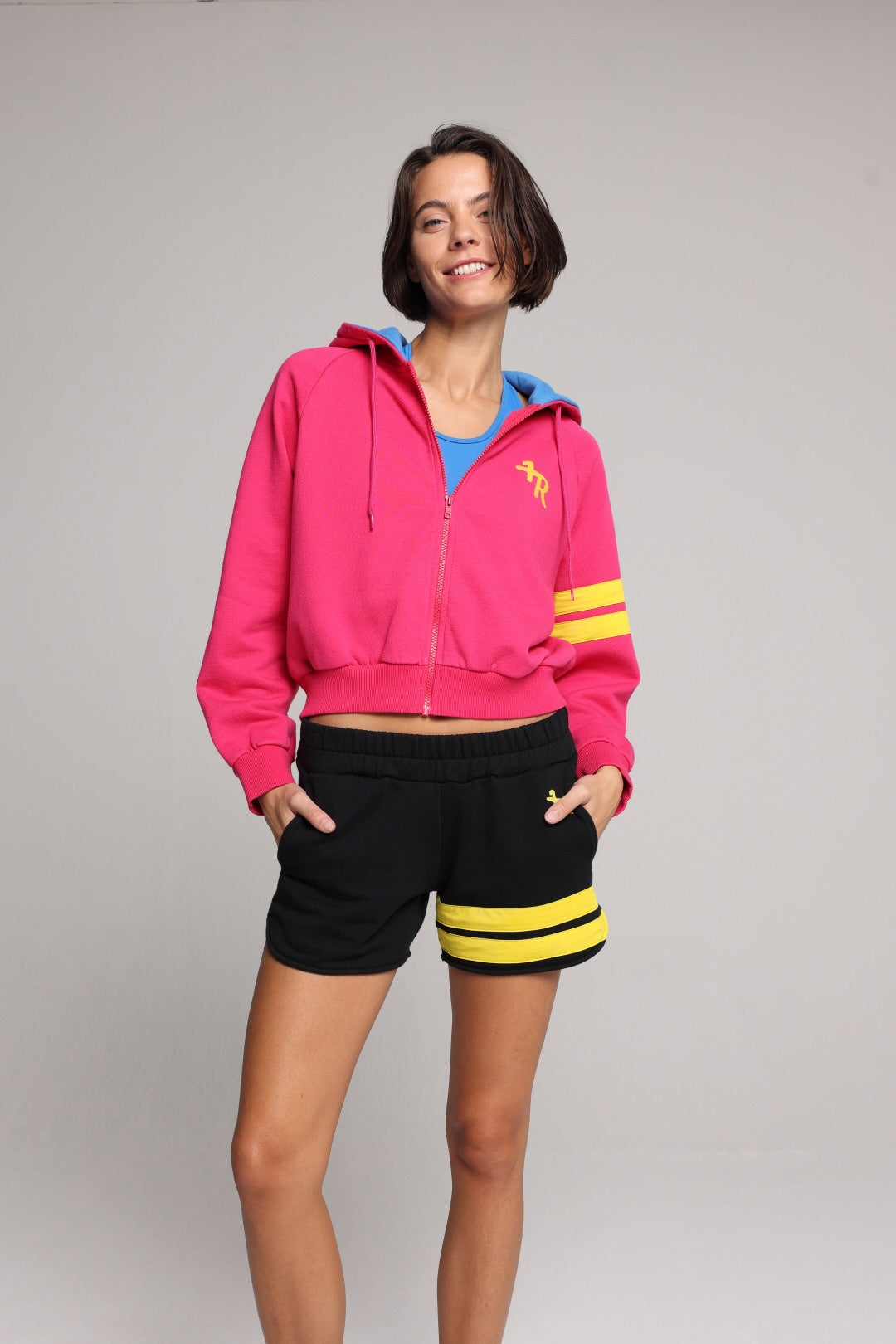 woman wearing a premium cotton pink hoodie with a blue hood and black shorts with yellow stripes by one more reason studio set up