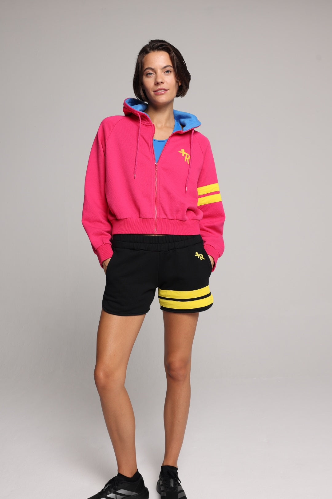 woman wearing a premium cotton pink hoodie with a blue hood and black shorts with yellow stripes by one more reason studio set up