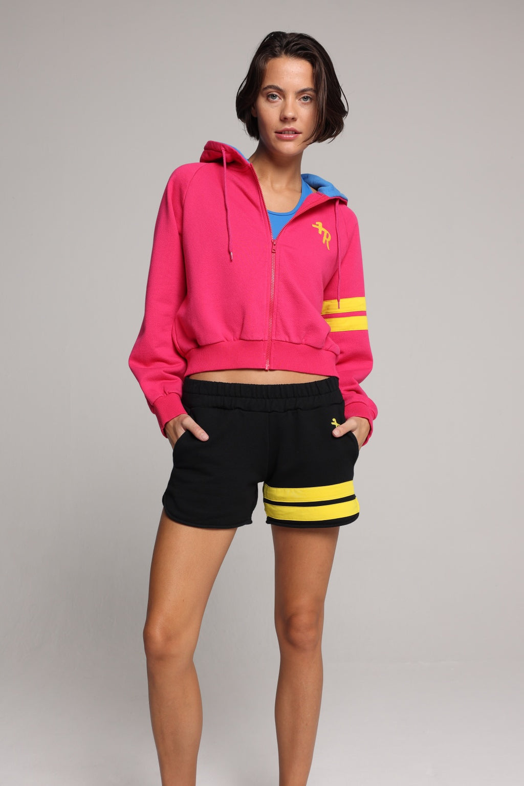 woman wearing a premium cotton pink hoodie with a blue hood and black shorts with yellow stripes by one more reason studio set up