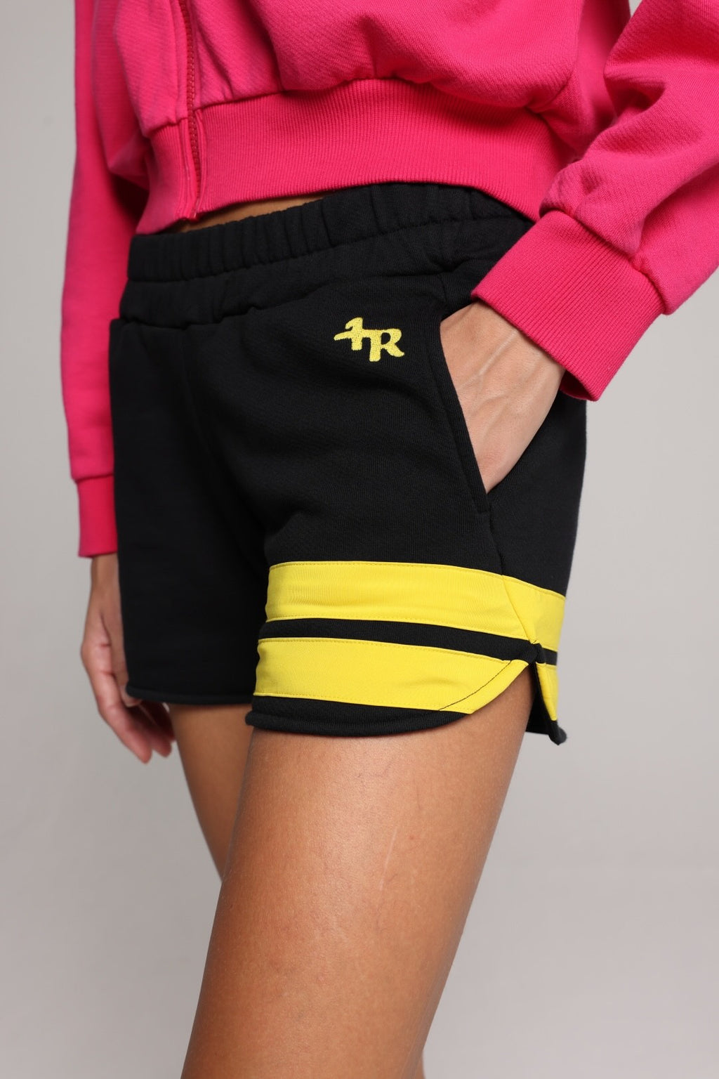 woman wearing a premium cotton pink hoodie with a blue hood and black shorts with yellow stripes by one more reason studio set up