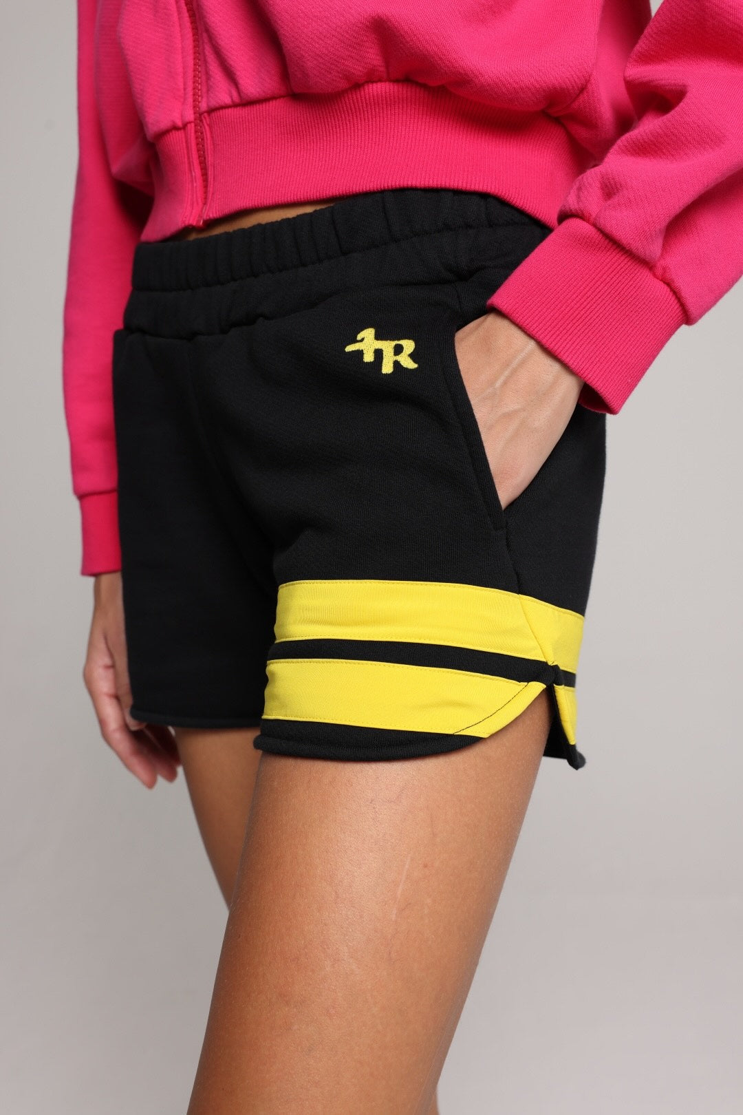 woman wearing a premium cotton pink hoodie with a blue hood and black shorts with yellow stripes by one more reason studio set up