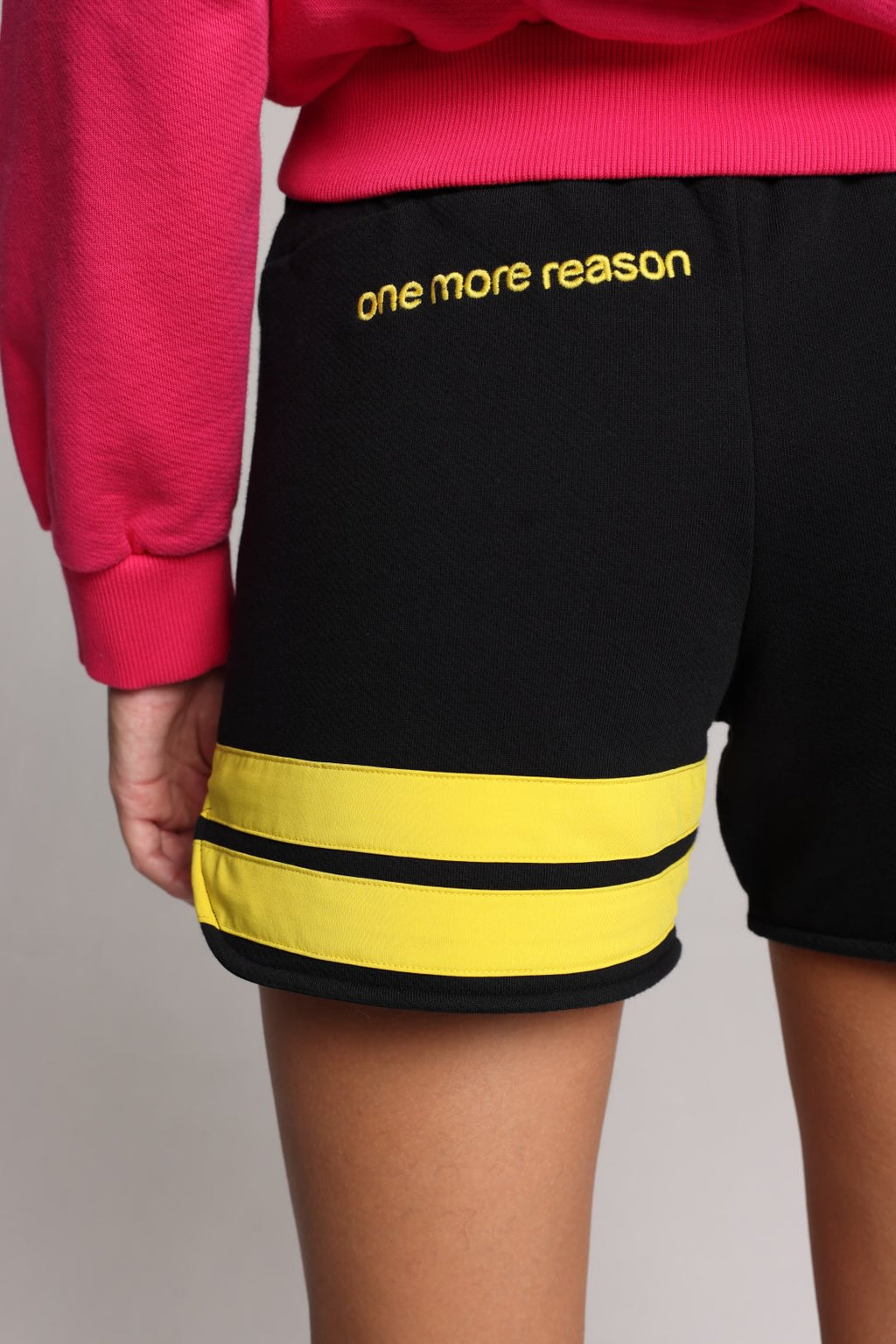 woman wearing black shorts with yellow stripes by one more reason studio set up back view