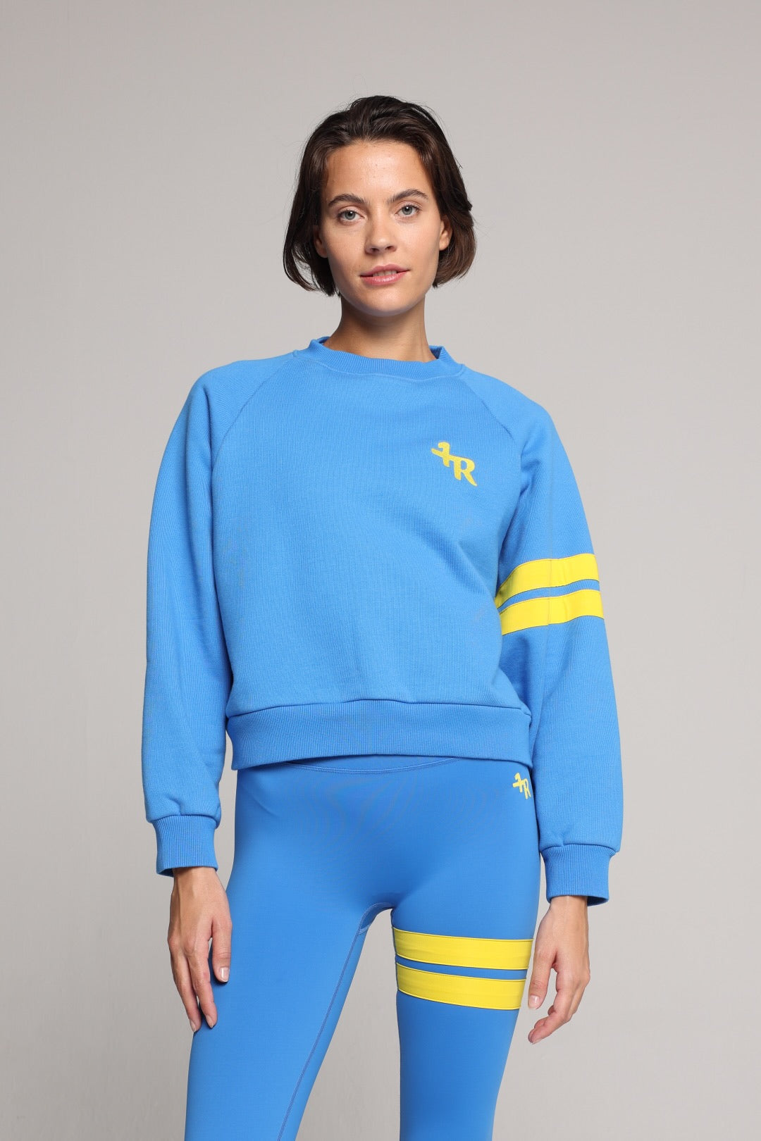 Woman wearing blue high-waisted leggings and oversized  blue crew sweater with yellow stripes by One More Reason, studio fashion.