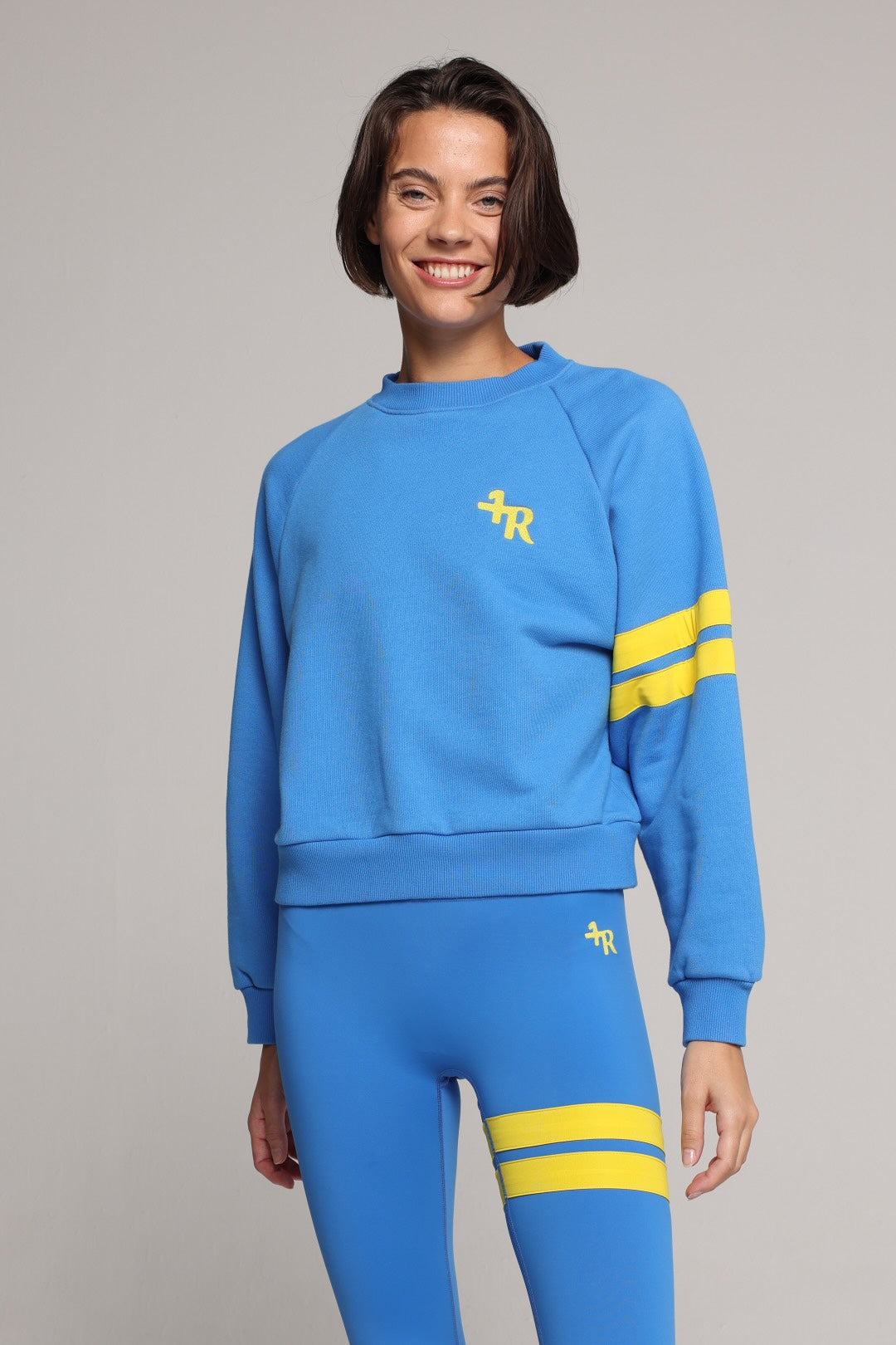 woman wearing blue high-waisted leggings and oversized  blue crew sweater with yellow stripes by One More Reason, studio shot