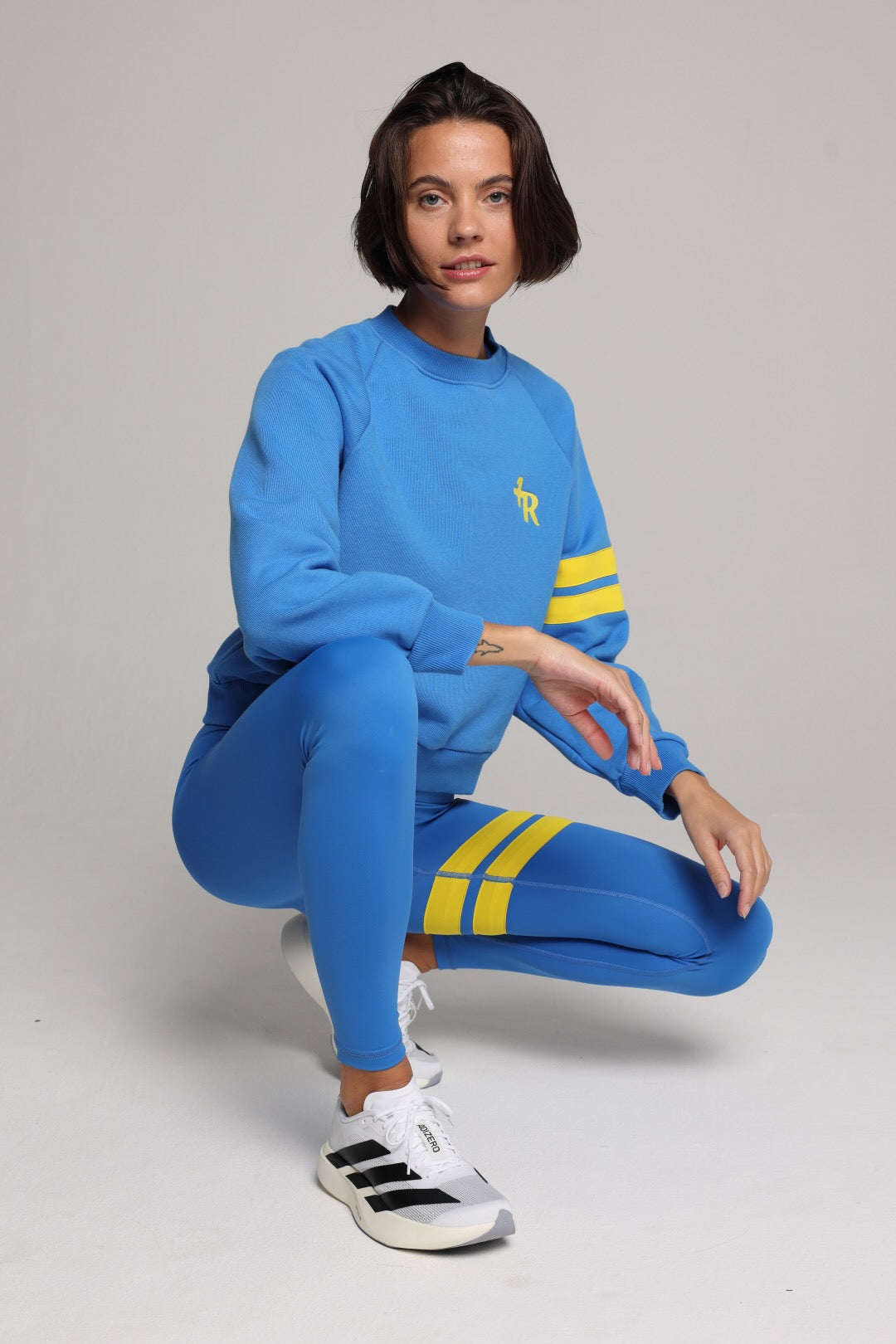 Woman wearing blue high-waisted leggings and oversized  blue crew sweater with yellow stripes by One More Reason, studio fashion.
