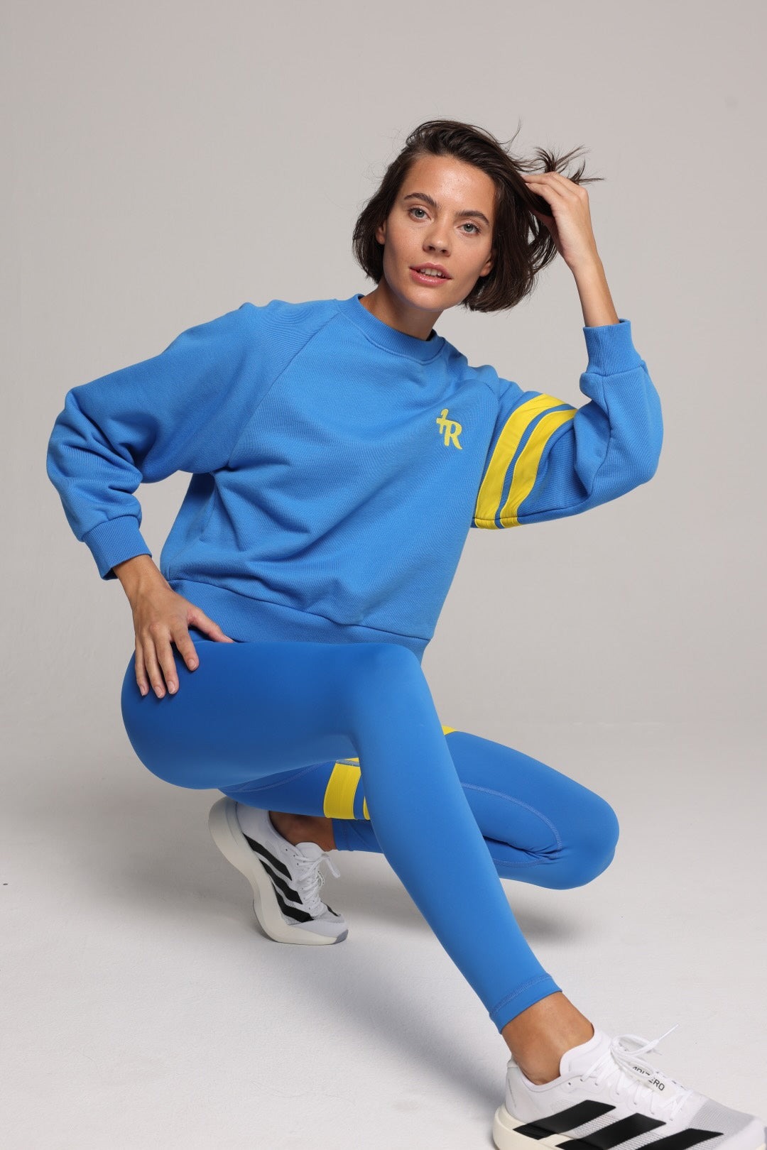 Woman wearing blue high-waisted leggings and oversized  blue crew sweater with yellow stripes by One More Reason, studio fashion.