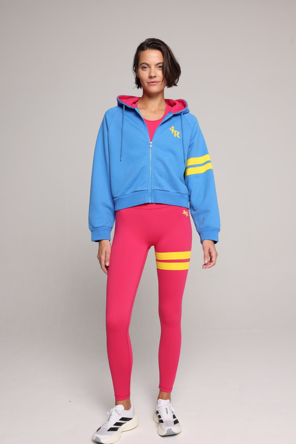 Woman wearing a blue hoodie and pink leggings with yellow stripes on a gray background

