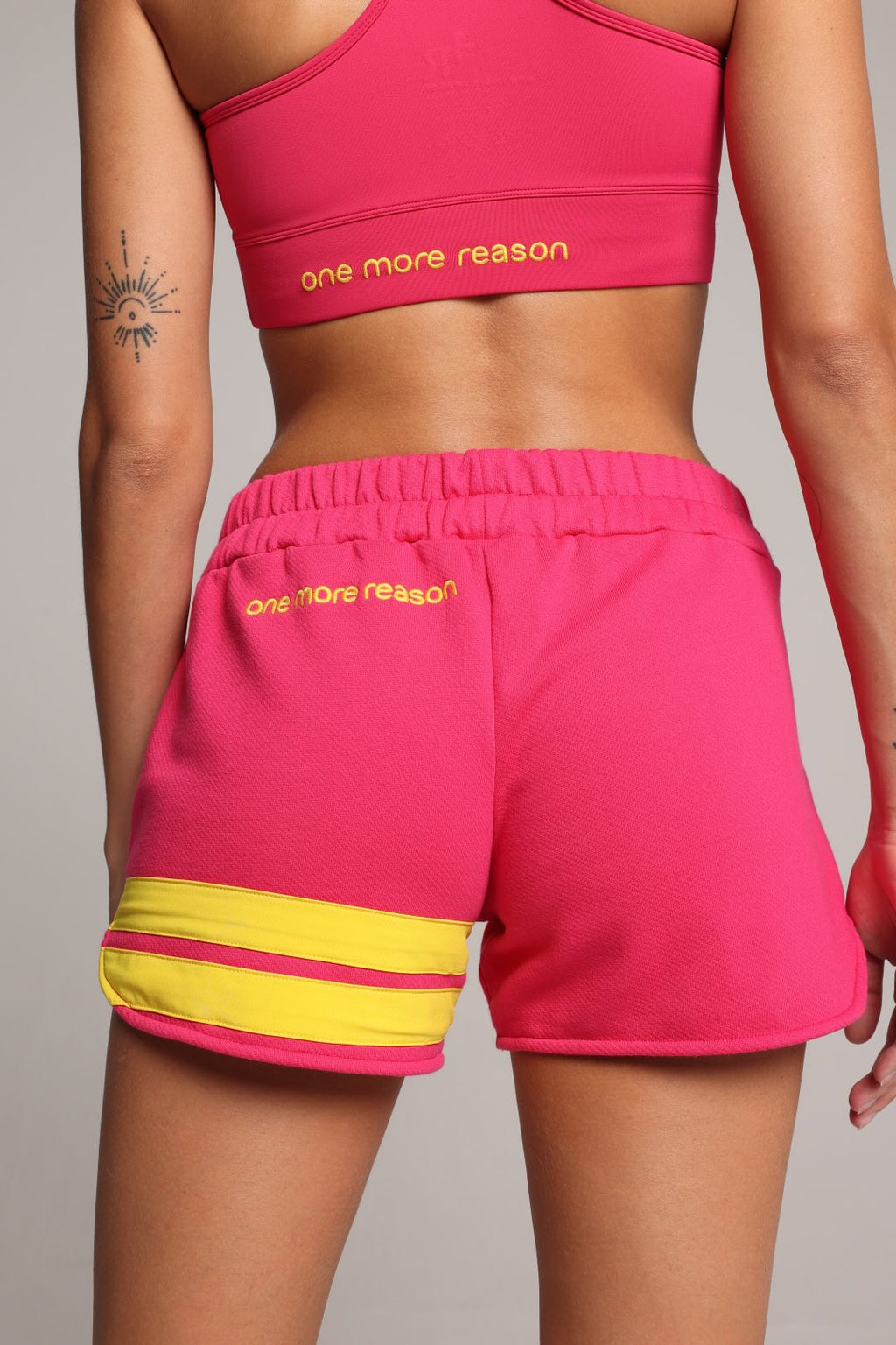 woman wearing pink cotton shorts with yellow stripes by one more reason premium sportswear studio set back view