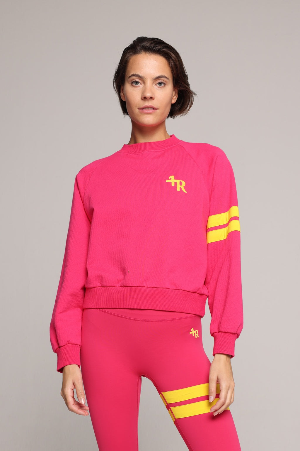 A woman wearing a bright pink sweater and leggings with yellow stripes by One More Reason, the premium sportswear brand made in Europe in a studio setting 