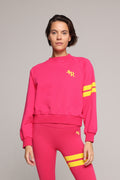A woman wearing a bright pink sweater and leggings with yellow stripes by One More Reason, the premium sportswear brand made in Europe in a studio setting 