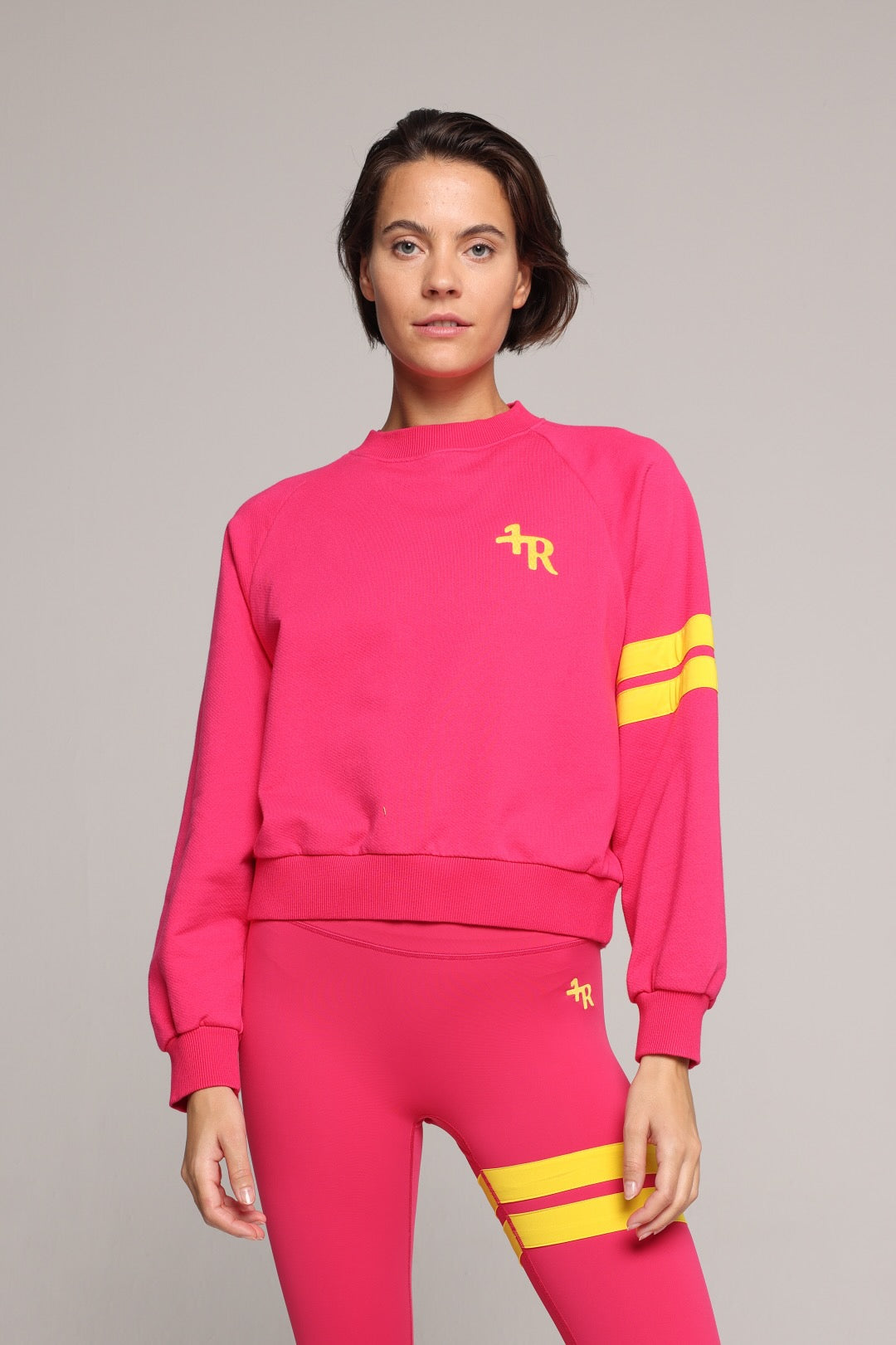 A woman wearing a bright pink sweater and leggings with yellow stripes by One More Reason, the premium sportswear brand made in Europe in a studio setting 