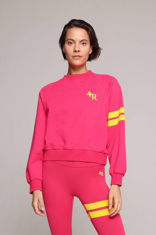A woman wearing a bright pink sweater and leggings with yellow stripes by One More Reason, the premium sportswear brand made in Europe in a studio setting 