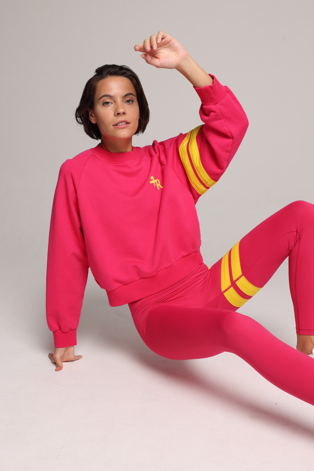 A woman wearing a bright pink sweater and leggings with yellow stripes by One More Reason, the premium sportswear brand made in Europe in a studio setting 