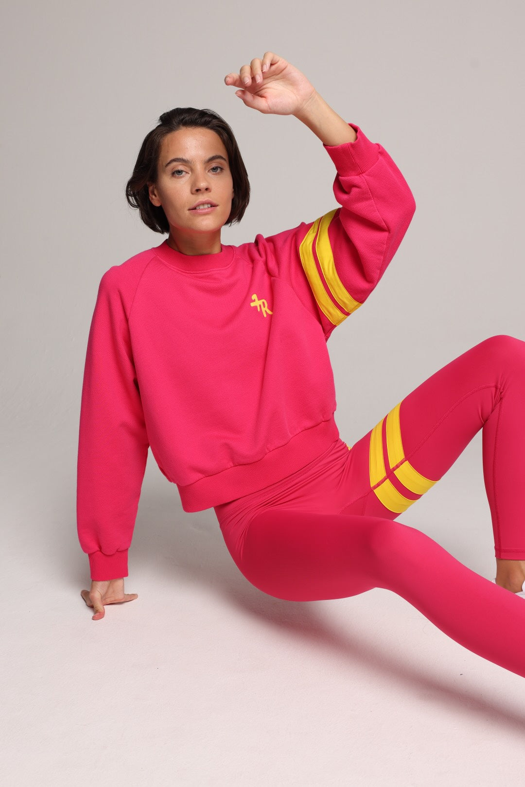 A woman wearing a bright pink sweater and leggings with yellow stripes by One More Reason, the premium sportswear brand made in Europe in a studio setting 