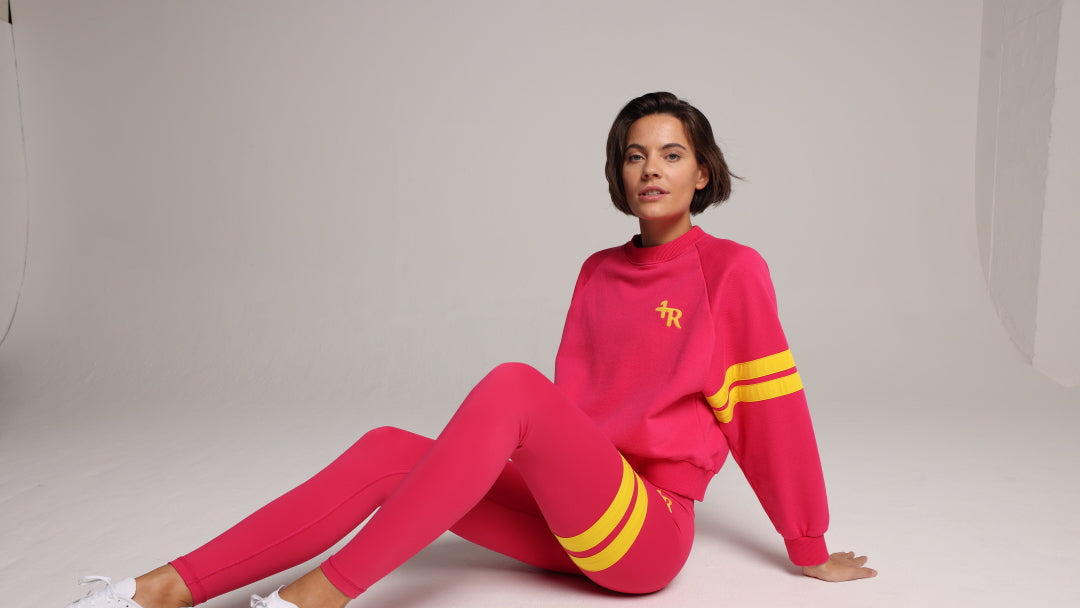 Woman wearing pink leggings and a pink sweater with yellow stripes by one more reason in a studio set