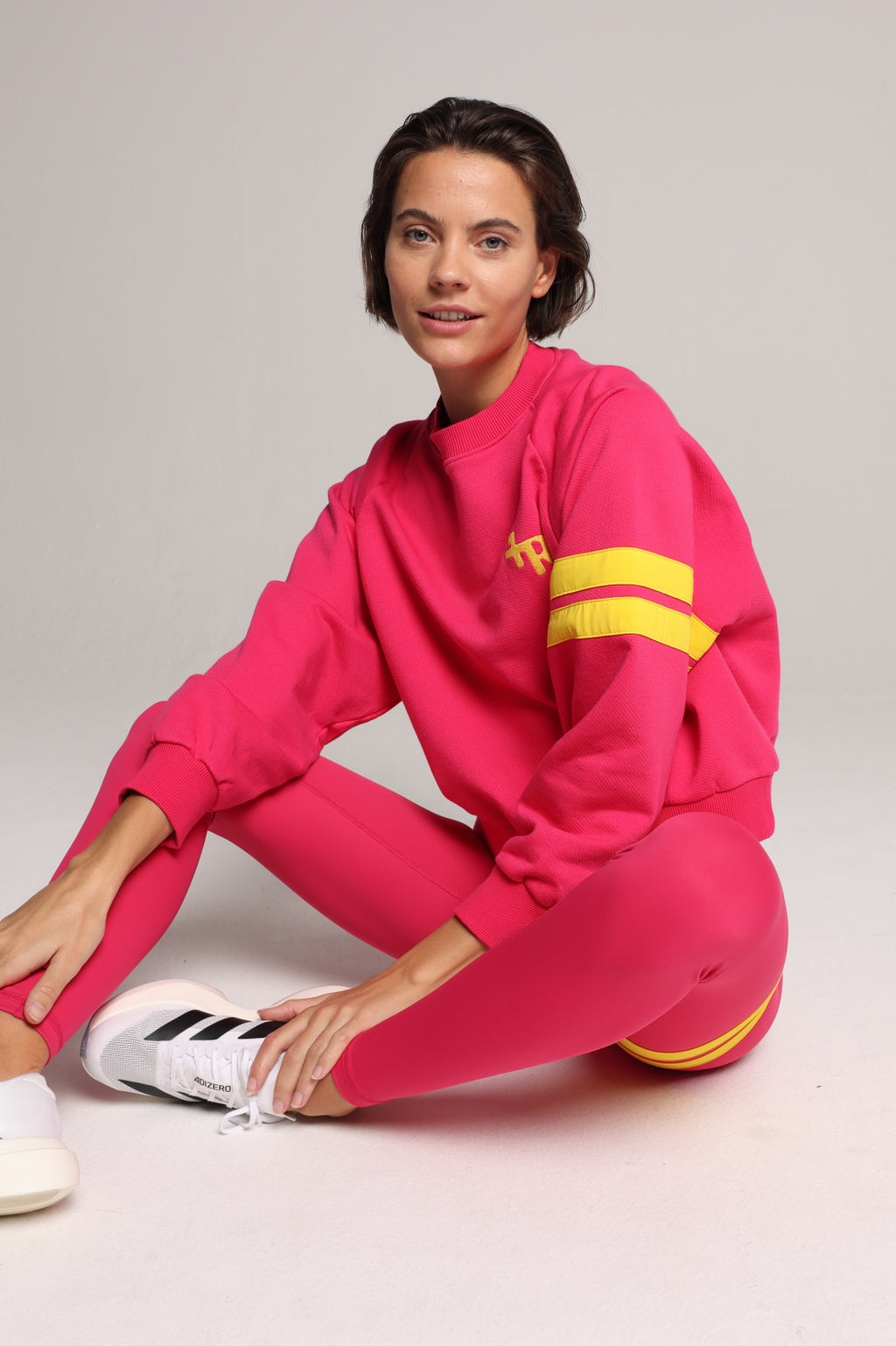 A woman wearing a bright pink sweater and leggings with yellow stripes by One More Reason, the premium sportswear brand made in Europe in a studio setting 