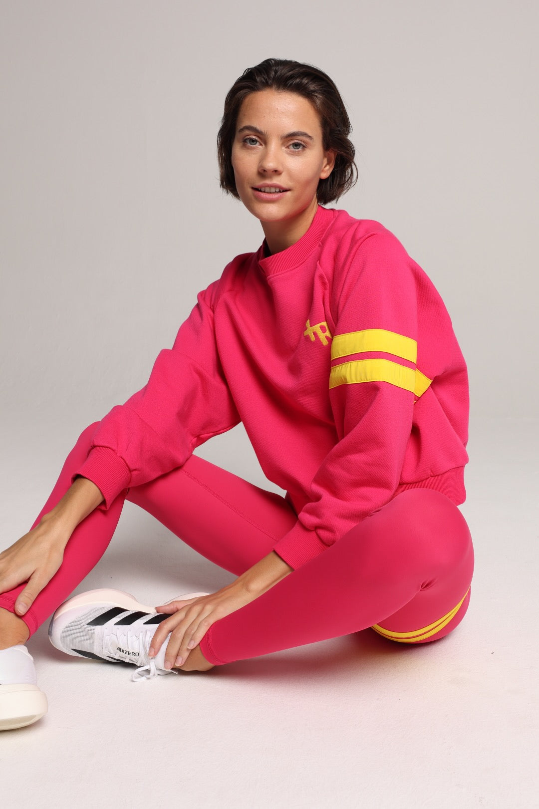 A woman wearing a bright pink sweater and leggings with yellow stripes by One More Reason, the premium sportswear brand made in Europe in a studio setting 