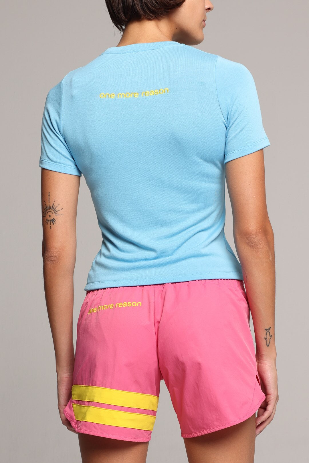 Woman in blue t-shirt and pink shorts with yellow stripes by one more reason studio set back view