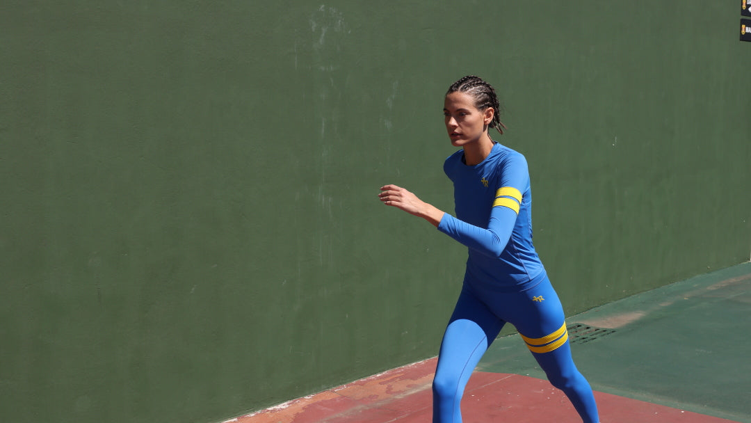 woman in a premium blue athletic outfit  with yellow stripes by One More Reason running on a track with a green wall in the background