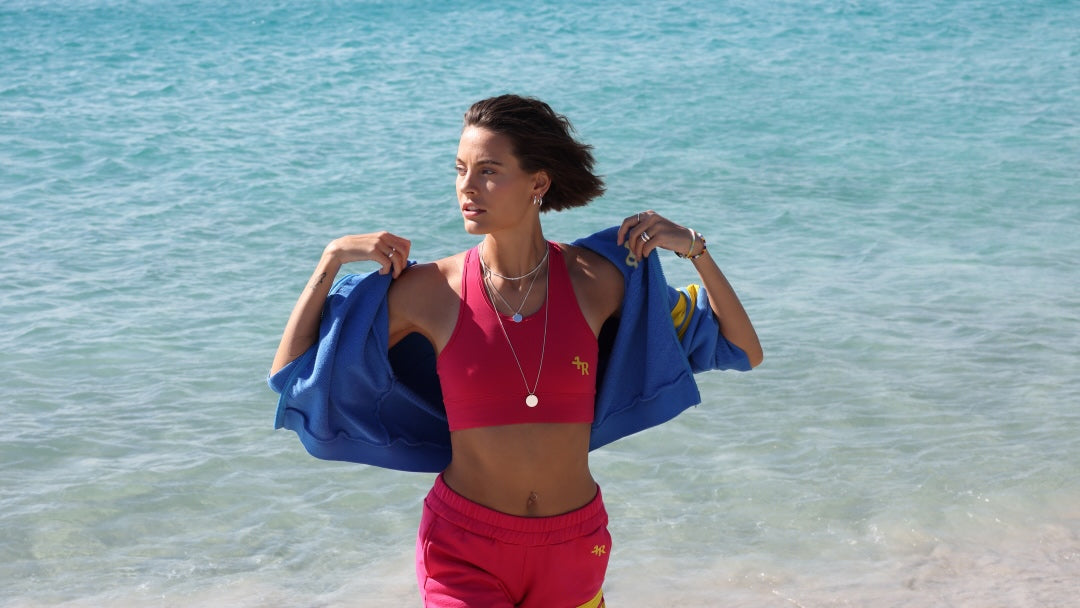 woman wearing a blue jacket and pink shorts with yellow stripes by one more reason running on a beach
