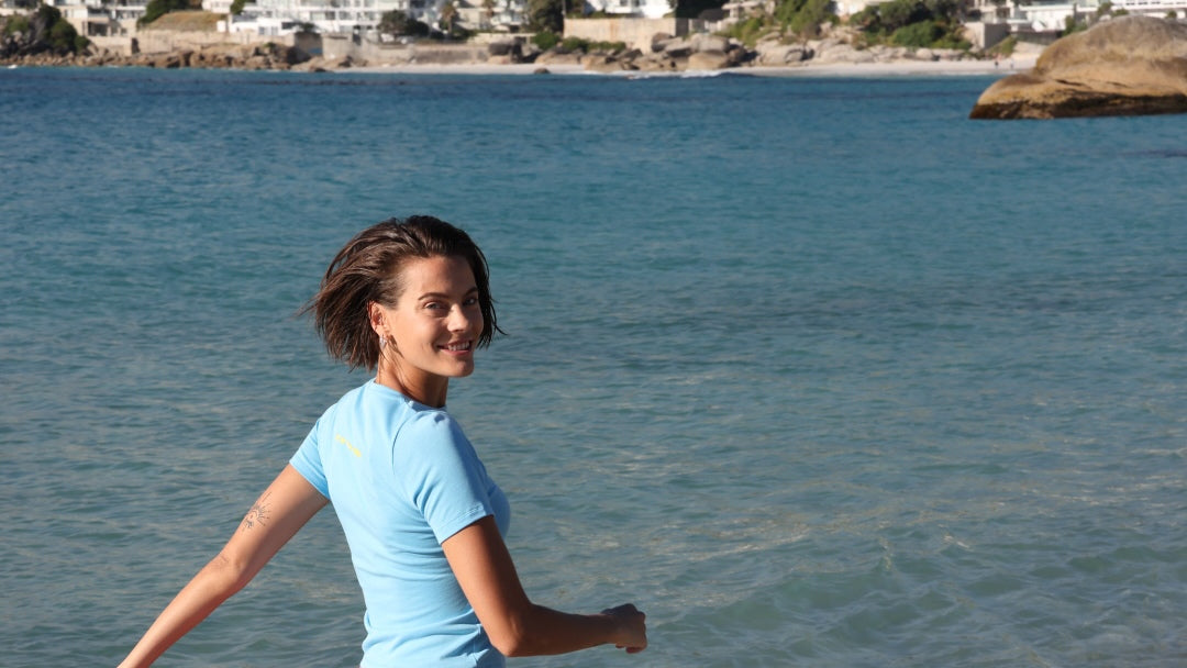 Woman in blue shirt and pink shorts with yellow stripes by one more reason walking on a beach with clear blue sky and ocean
