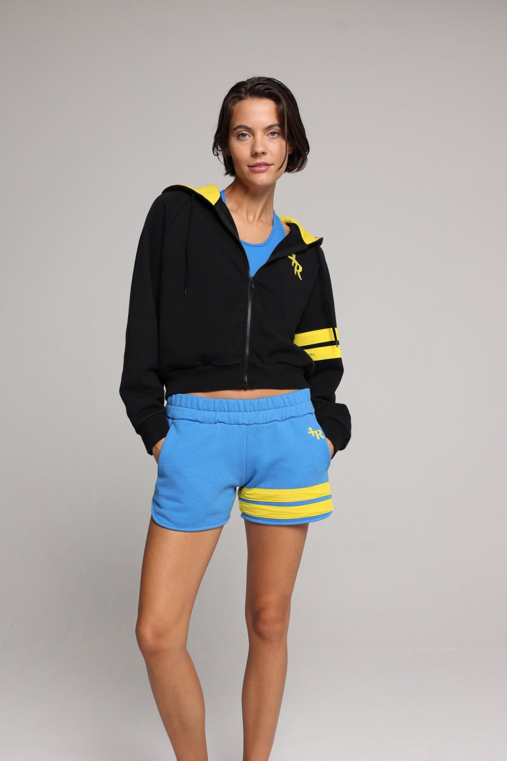 Woman wearing a black hoodie with yellow stripes and blue shorts by one more reason studio set
