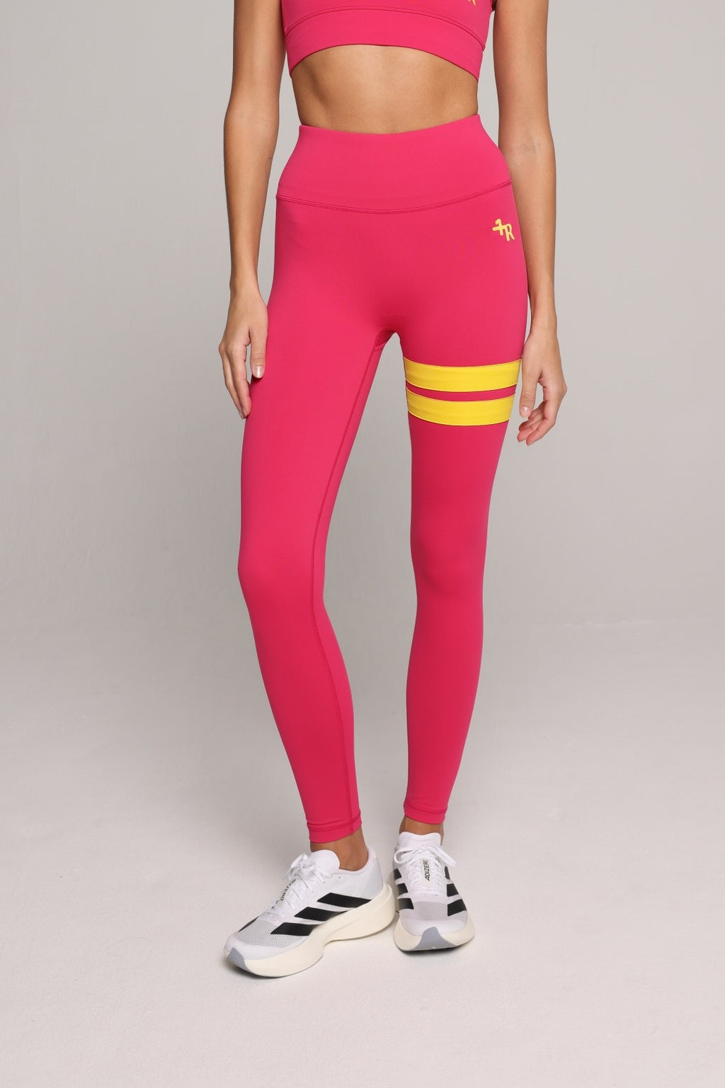 A woman wearing a bright pink leggings with yellow stripes by One More Reason, the premium sportswear brand made in Europe in a studio setting 
