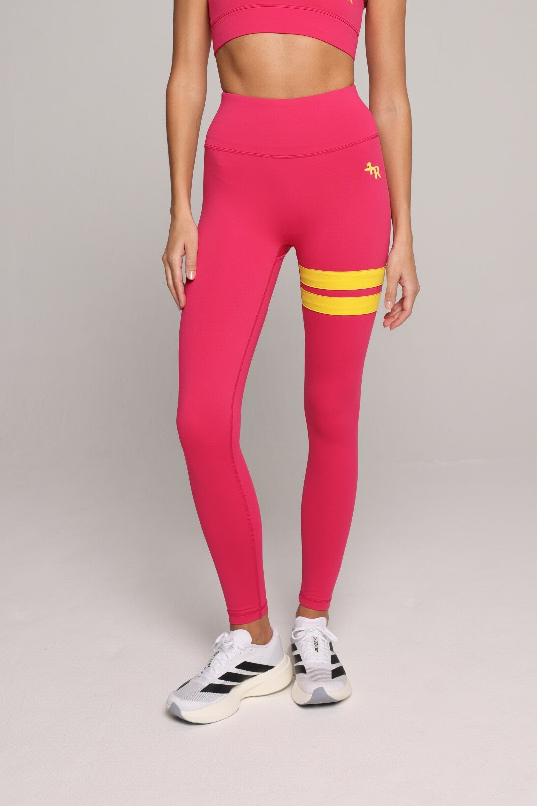 A woman wearing a bright pink leggings with yellow stripes by One More Reason, the premium sportswear brand made in Europe in a studio setting 