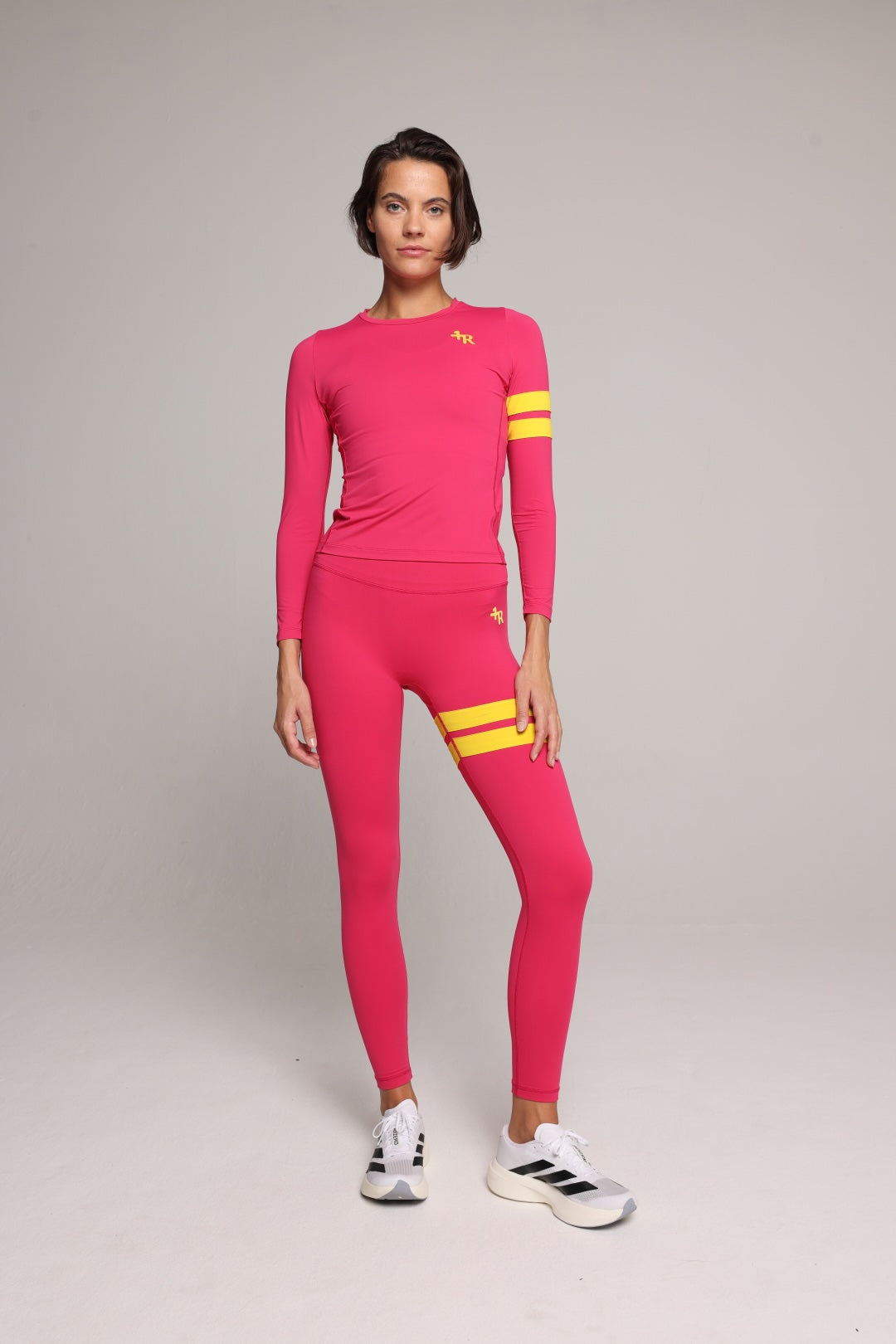 A woman wearing a bright pink performance sleeve and leggings with yellow stripes by One More Reason, the premium sportswear brand made in Europe in a studio setting 