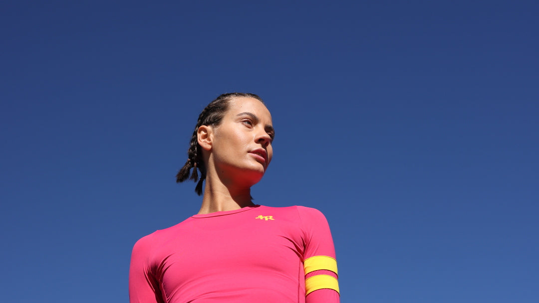 woman wearing a pink athletic outfit with yellow stripes by one more reason against a clear blue sky