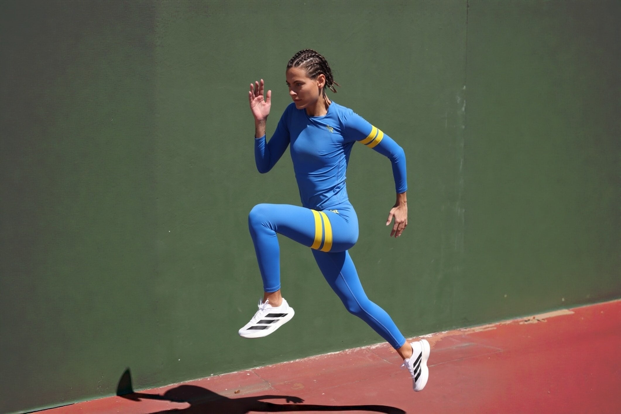woman in blue leggings and blue long sleeve shirt with yellow stripes by one more reason running on a green surface in  outdoor