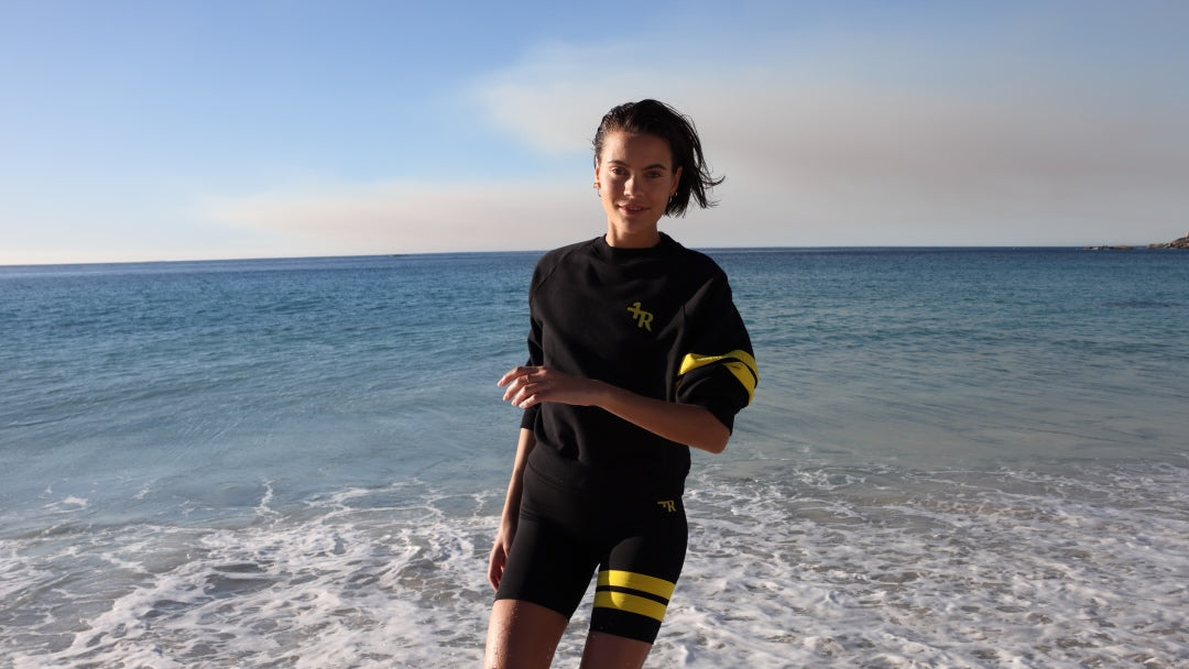 Woman by the ocean wearing a black sweater and sport shorts with yellow accents by one more reason