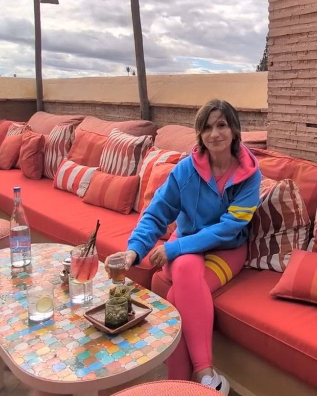 Founder of premium sports fashion brand one more reason sitting on a rooftop terrace in Marrakech wearing a pink leggings and a bicolor blue and pink hoodie with yellow signature stripes