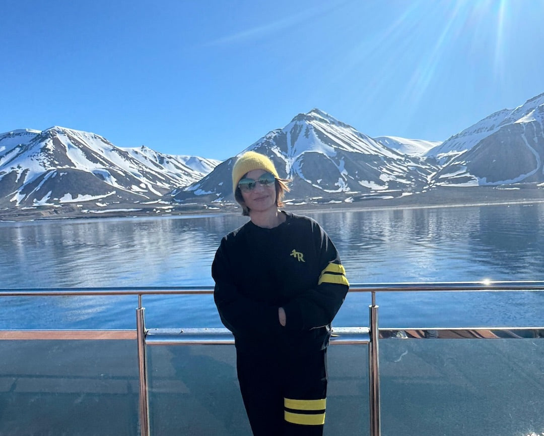 woman in a premium black sports outfit with yellow stripes from One More Reason standing on a boat deck with snow-covered mountains in the background